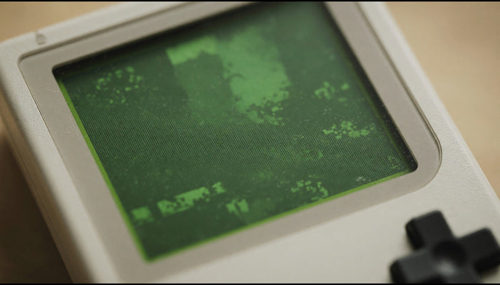 Gros plan sur l'écran d'une console rétro portable, lueur verte phosphore et grille de pixels visible.